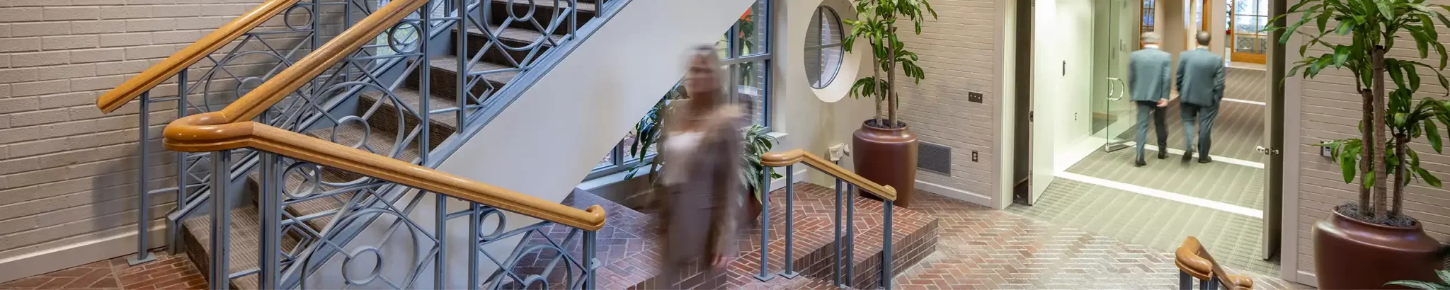 Woman walking up the office stairway while two men walk in the background