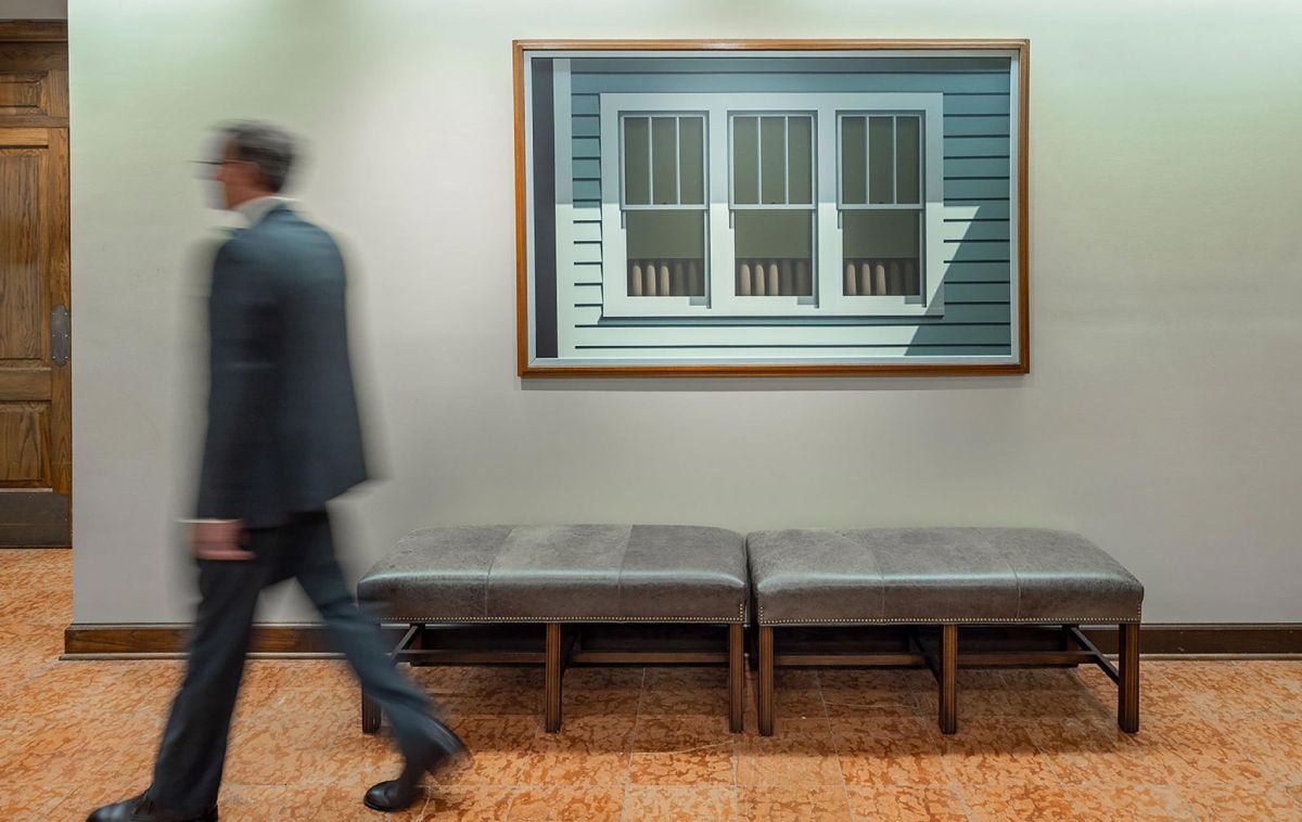 A man walking in the office corridor with a painting of a window on the wall.